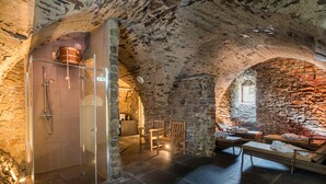 A stone-walled bathroom with a glass shower enclosure, wooden chairs, and a seating area with a stone fireplace. - Schlosshotel Purschenstein (Neuhausen)