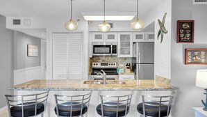 Una cocina con isla central, taburetes de bar, microondas, horno y refrigerador.
