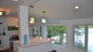 Une cuisine moderne dotée d’un plan de travail en marbre, de luminaires suspendus et de grandes fenêtres donnant sur un lac.