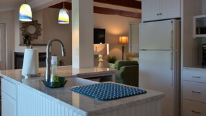 Une cuisine moderne dotée d’un plan de travail en marbre, d’un évier encastré, d’un réfrigérateur, de luminaires suspendus et d’un coin repas avec une chaise et une table.
