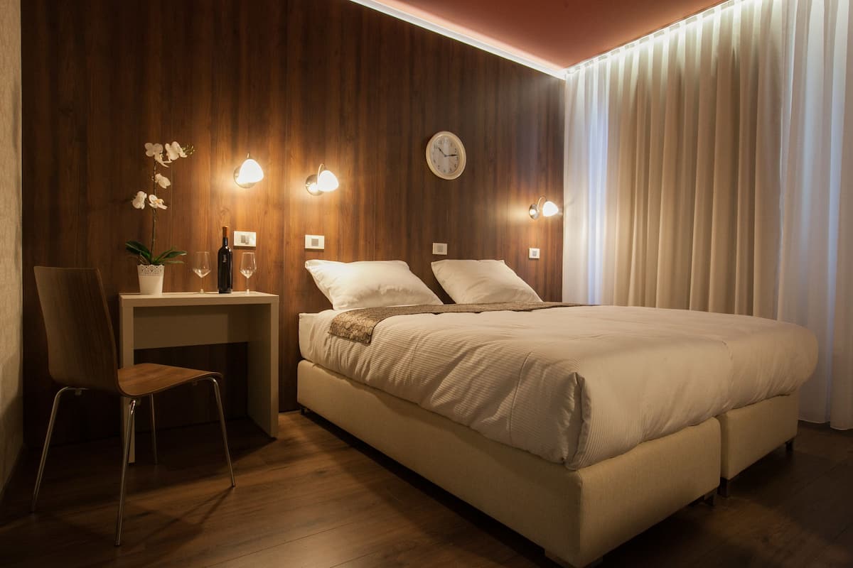 A bedroom with a bed, a desk, a chair, and a potted plant.