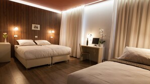 Ein Hotelzimmer mit einer Wand im Holzoptik, einem Bett mit weißer Bettwäsche, einem Schreibtisch mit Computer und einem kleinen Topfpflanzen.