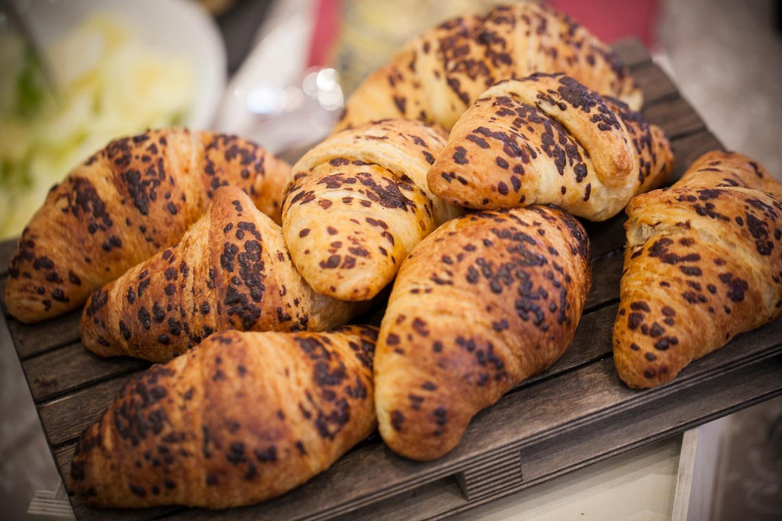 A tray of golden-brown pastries with dark spots, likely croissants, on a wooden surface.