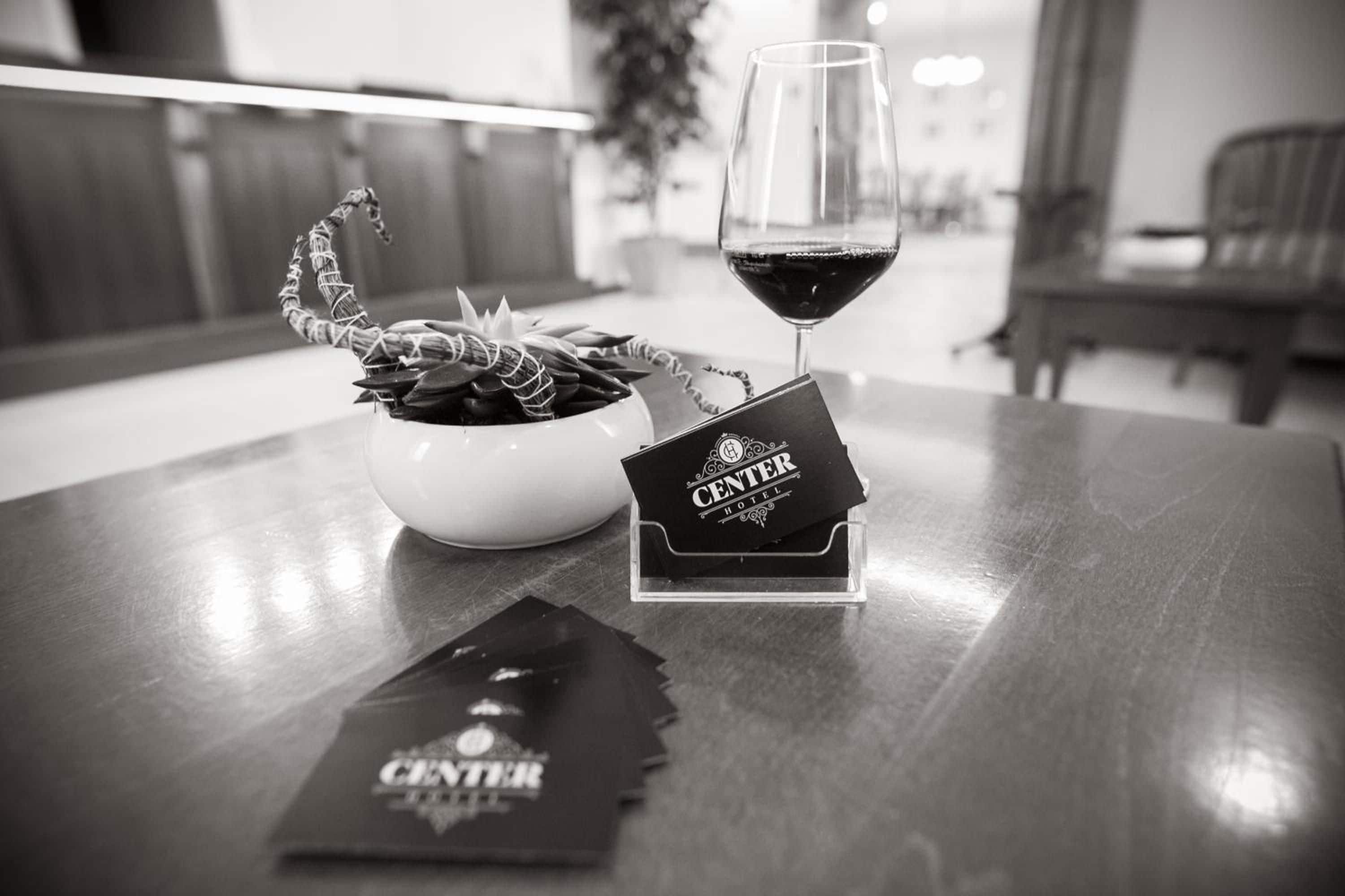 A hotel reception area with a glass of red wine, a decorative plant, and a Center Hotel brochure on a wooden table.