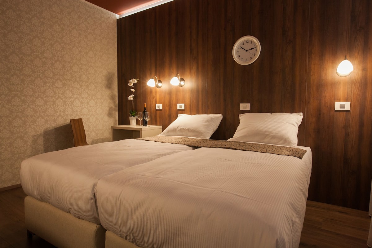 A double bed with a wooden headboard, a wall clock, and three wall-mounted lights.