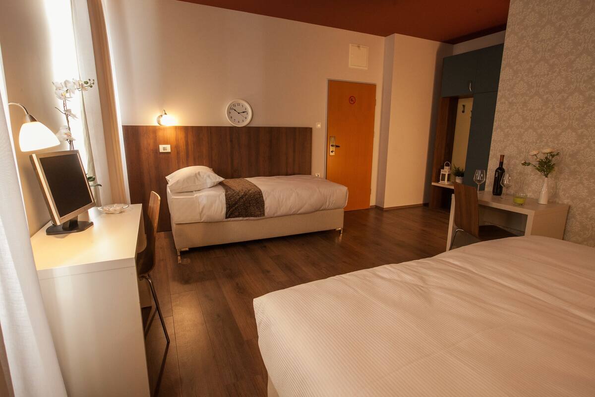 A hotel room with a bed, bedside table, lamp, and a clock on the wall.
