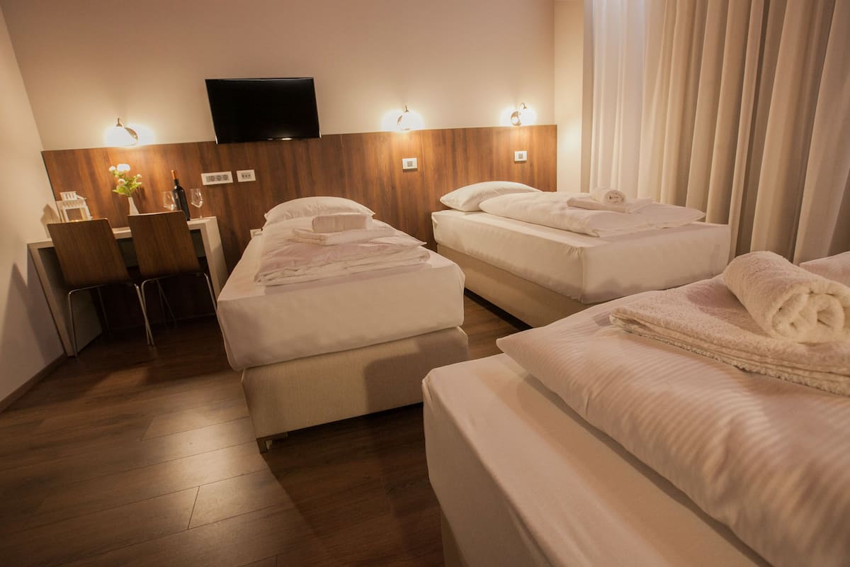 A hotel room with two beds, a desk with a chair, a flat-screen TV mounted on the wall, and a window with curtains.