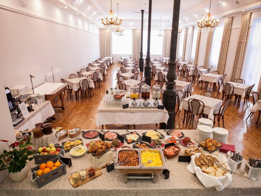 A large dining hall with multiple tables and chairs, a buffet with various food items, and decorative chandeliers.