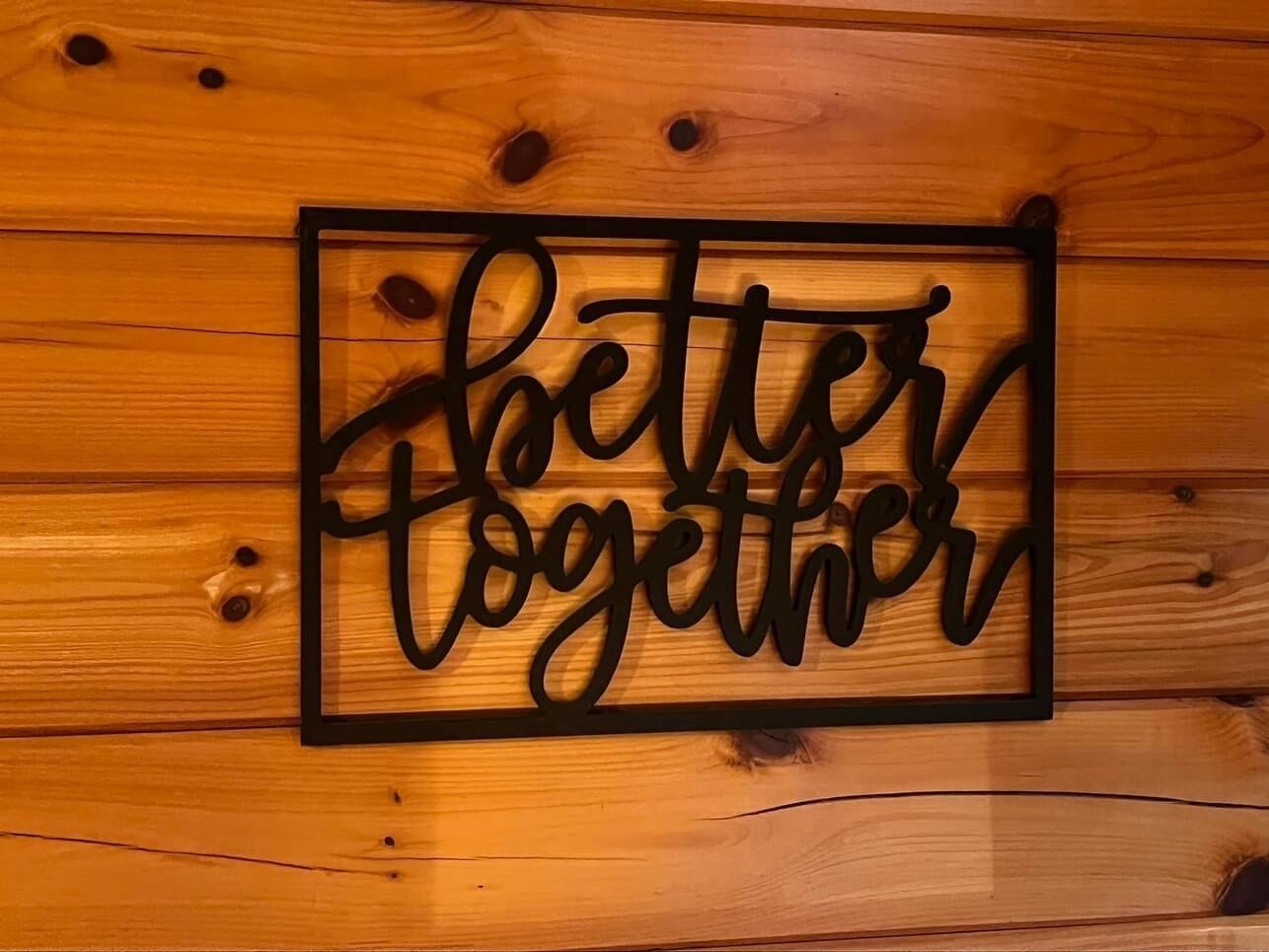 A wooden wall with a black metal sign that reads "Better Together."