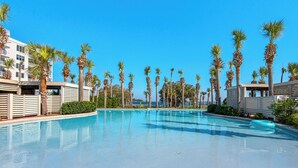 A clear blue pool surrounded by palm trees and modern buildings.