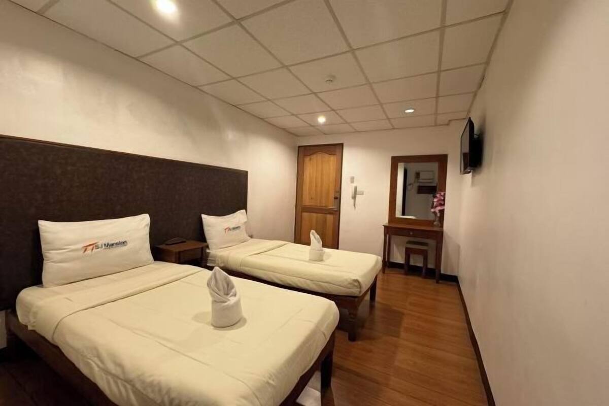 A hotel room with two beds, a wooden headboard, a small desk, and a mirror.