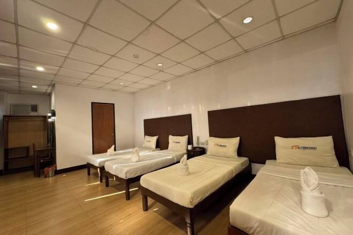A hotel room with three beds, a wooden floor, a tiled ceiling, and a wooden door.