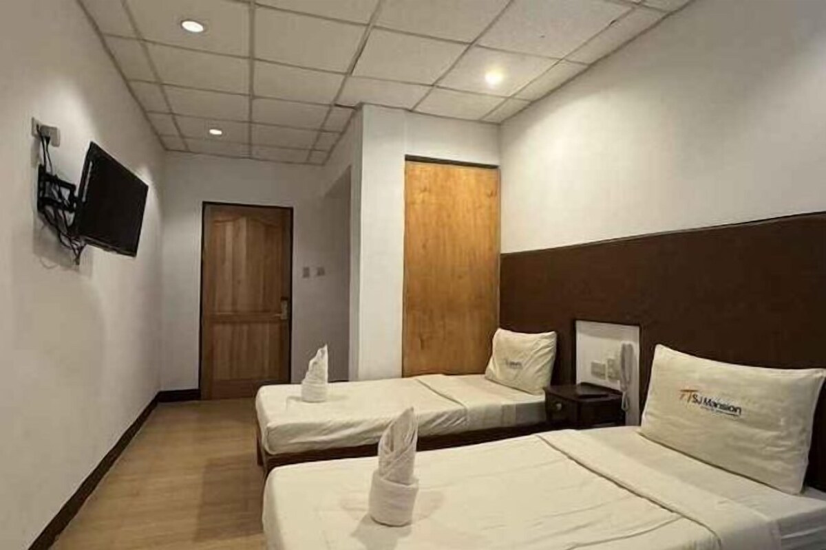 A hotel room with two single beds, a flat-screen TV mounted on the wall, a wooden door, and a framed picture on the wall.
