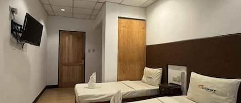 A hotel room with two single beds, a flat-screen TV mounted on the wall, a wooden door, and a framed picture on the wall.