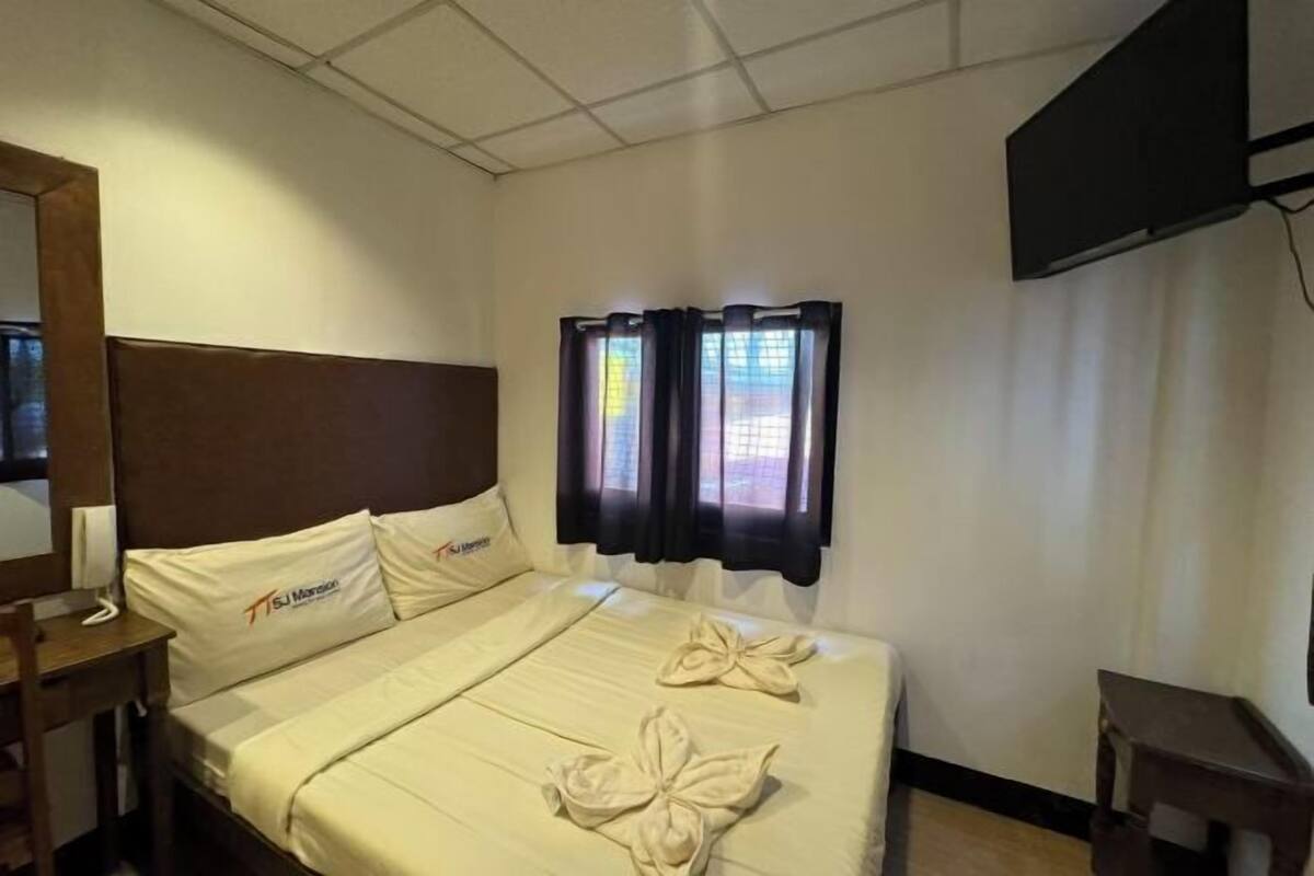 A hotel room with a bed, a TV mounted on the wall, and a window with curtains.