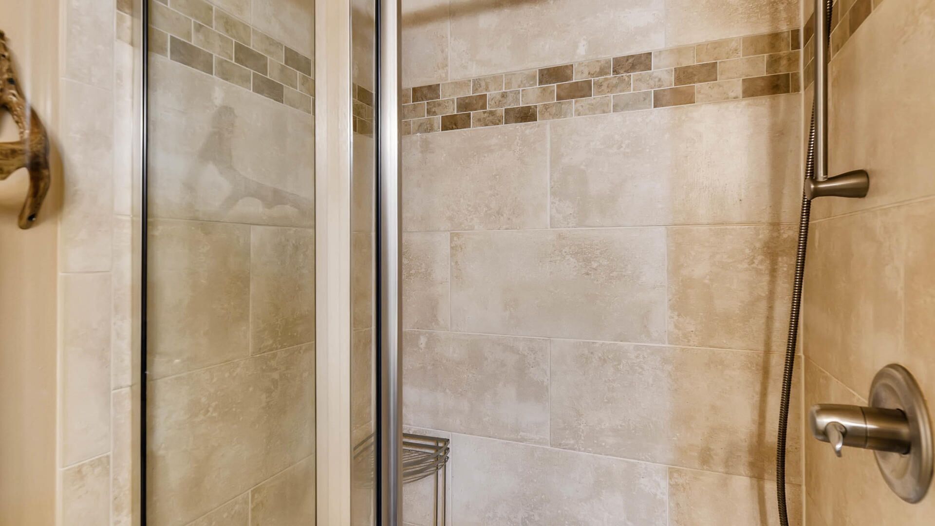 A shower area with a glass door, beige tiles, and a showerhead.