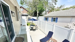 A covered patio with a sliding glass door, a small table with chairs, and two lounge chairs.