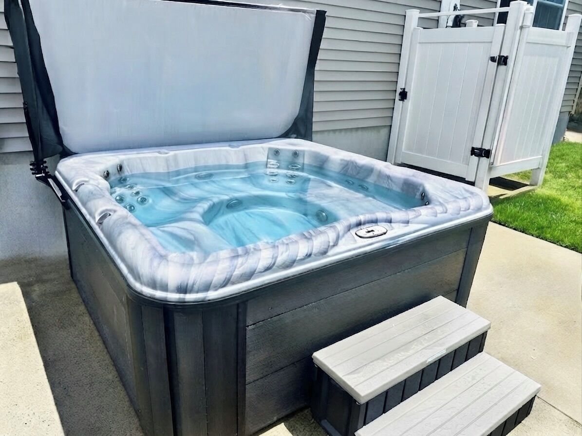 Ein Whirlpool mit Abdeckung, Stufen, die zu ihm führen, und ein weißer Zaun im Hintergrund.