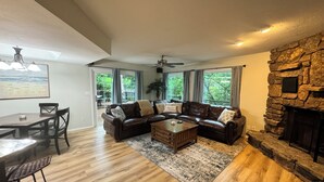 A living room with a stone fireplace, a sectional sofa, a dining table with chairs, and a view through large windows. - Monkey Island Waterfront with Dock and boat ramp right next to it. (Afton)