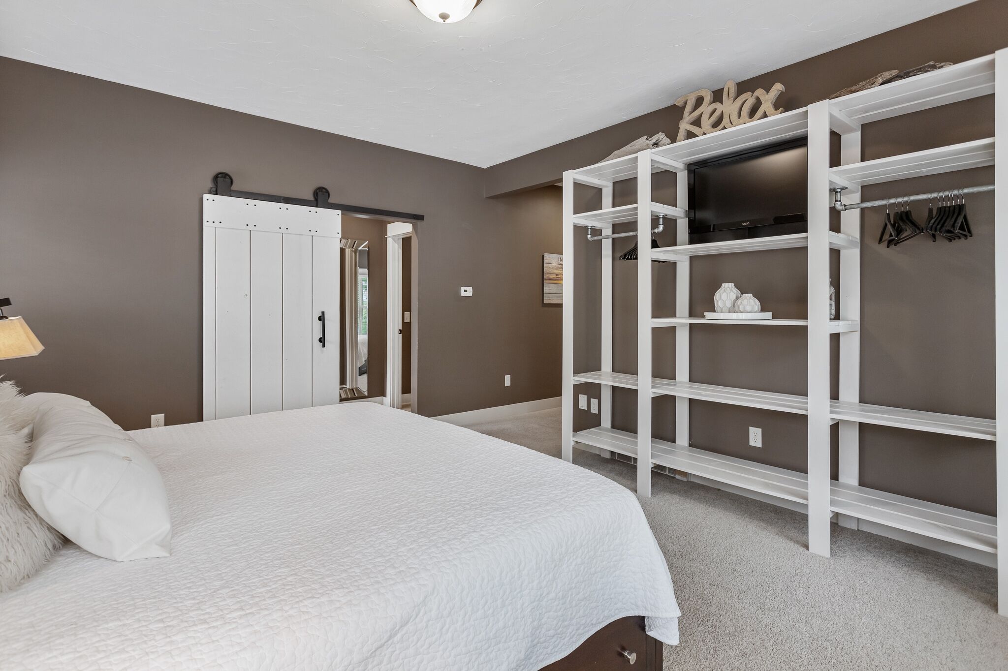 Une chambre avec un grand lit, une armoire avec espace pour suspendre les vêtements et une porte donnant sur une autre pièce.