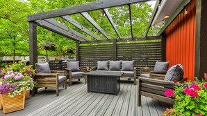 Un espace extérieur aménagé, abrité et doté de mobilier en bois et de jardinières fleuries.
