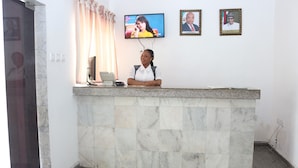 A reception desk with a marble counter, a television mounted above it, and two framed photographs on the wall. -  Crystalem Luxury Hotel (Uyo)