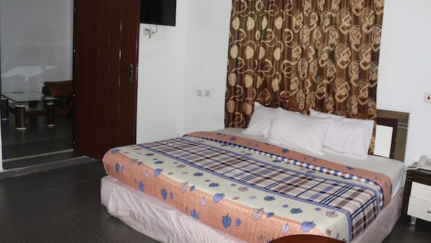 A hotel room with a bed, a television mounted on the wall, a curtain, and a door leading to a balcony. -  Crystalem Luxury Hotel (Uyo)