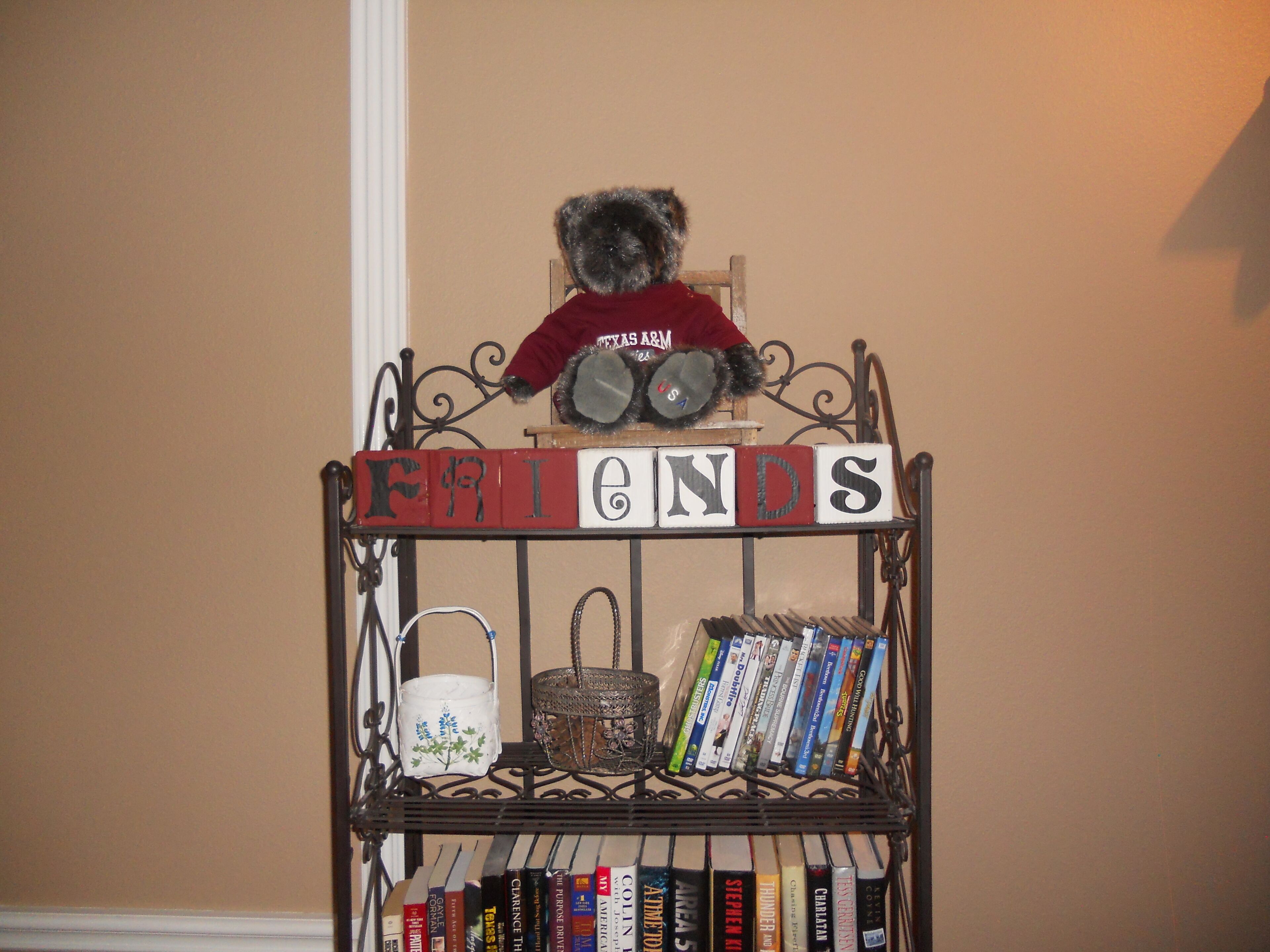 A metal bookshelf with a teddy bear on top and books and decorative items on the shelves.