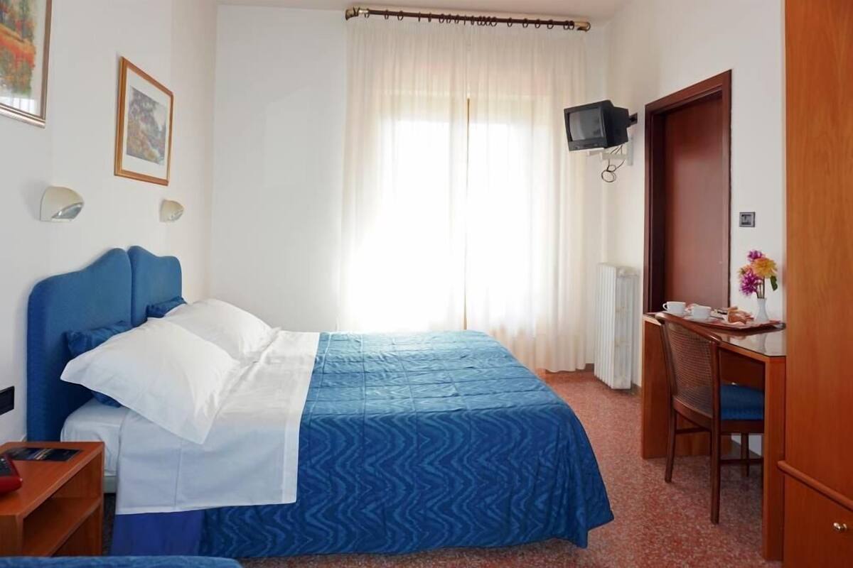 A hotel room with a bed, a desk, a chair, a television, and a door.