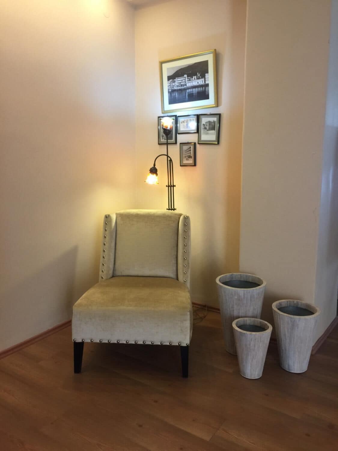 A corner room with a beige armchair, a floor lamp, and three wooden planters.