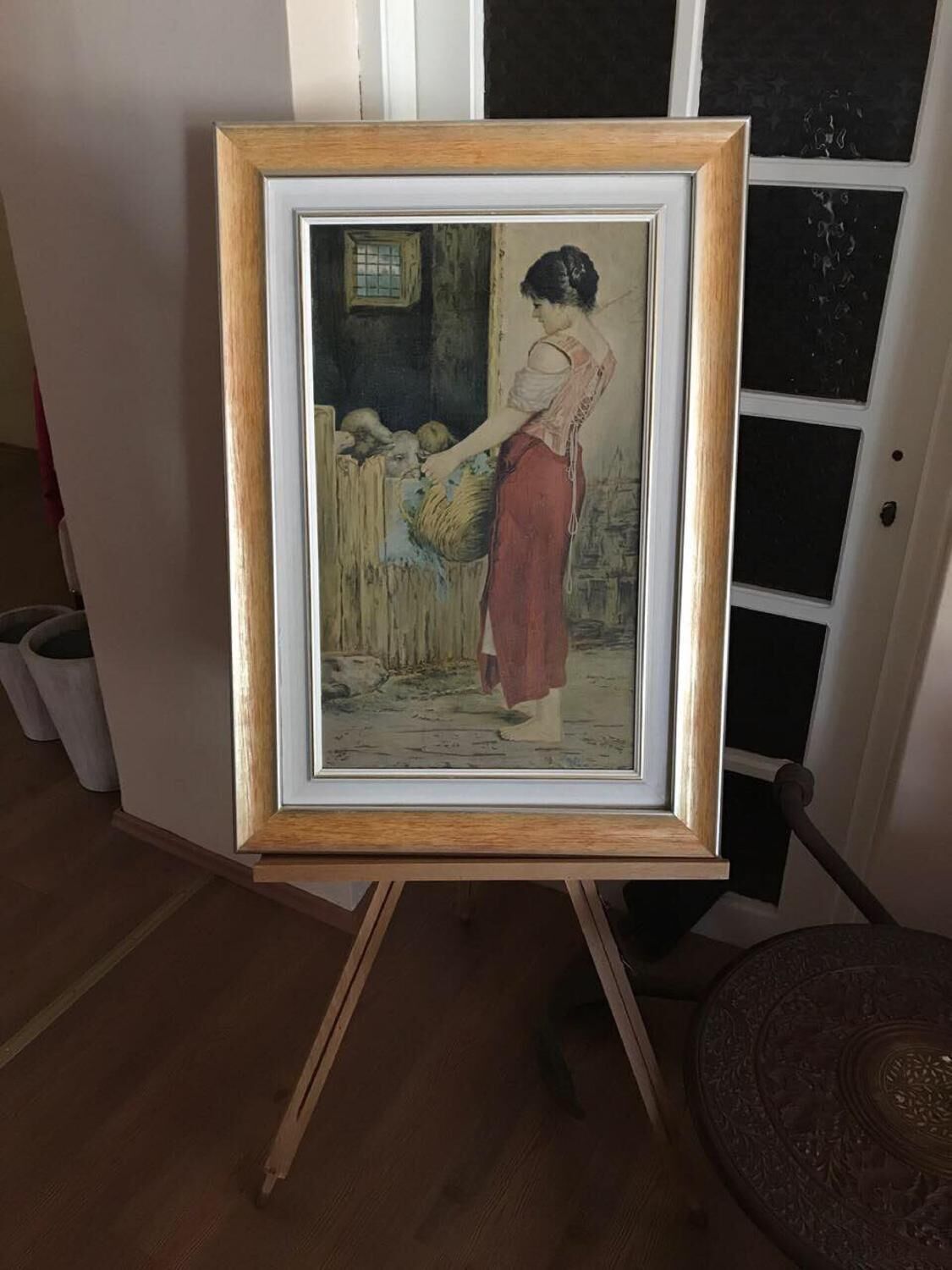 Una obra de arte enmarcadasobre un caballete en una habitación con suelo de madera y paredes blancas.