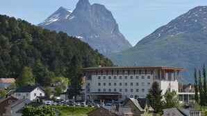 Un hotel con una imponente cadena montañosa al fondo, que presenta un edificio grande con numerosas ventanas y techo plano.