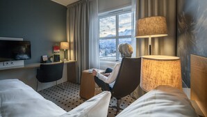 Una habitación de hotel con una cama, un escritorio con lámpara, una silla y un televisor.
