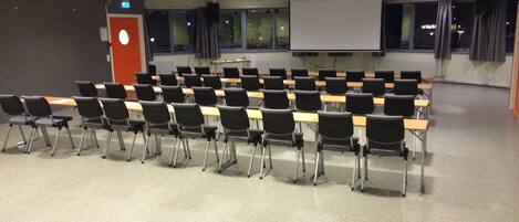 Une salle de classe avec des rangées de bureaux et de chaises, un écran de projection et un tableau blanc.