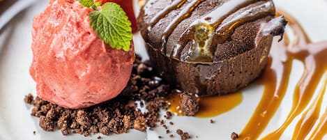 A dessert plate with a scoop of strawberry ice cream and a chocolate lava cake, both drizzled with caramel sauce.