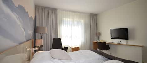 A hotel room with a large bed, a desk with a TV, a chair, and a lamp.