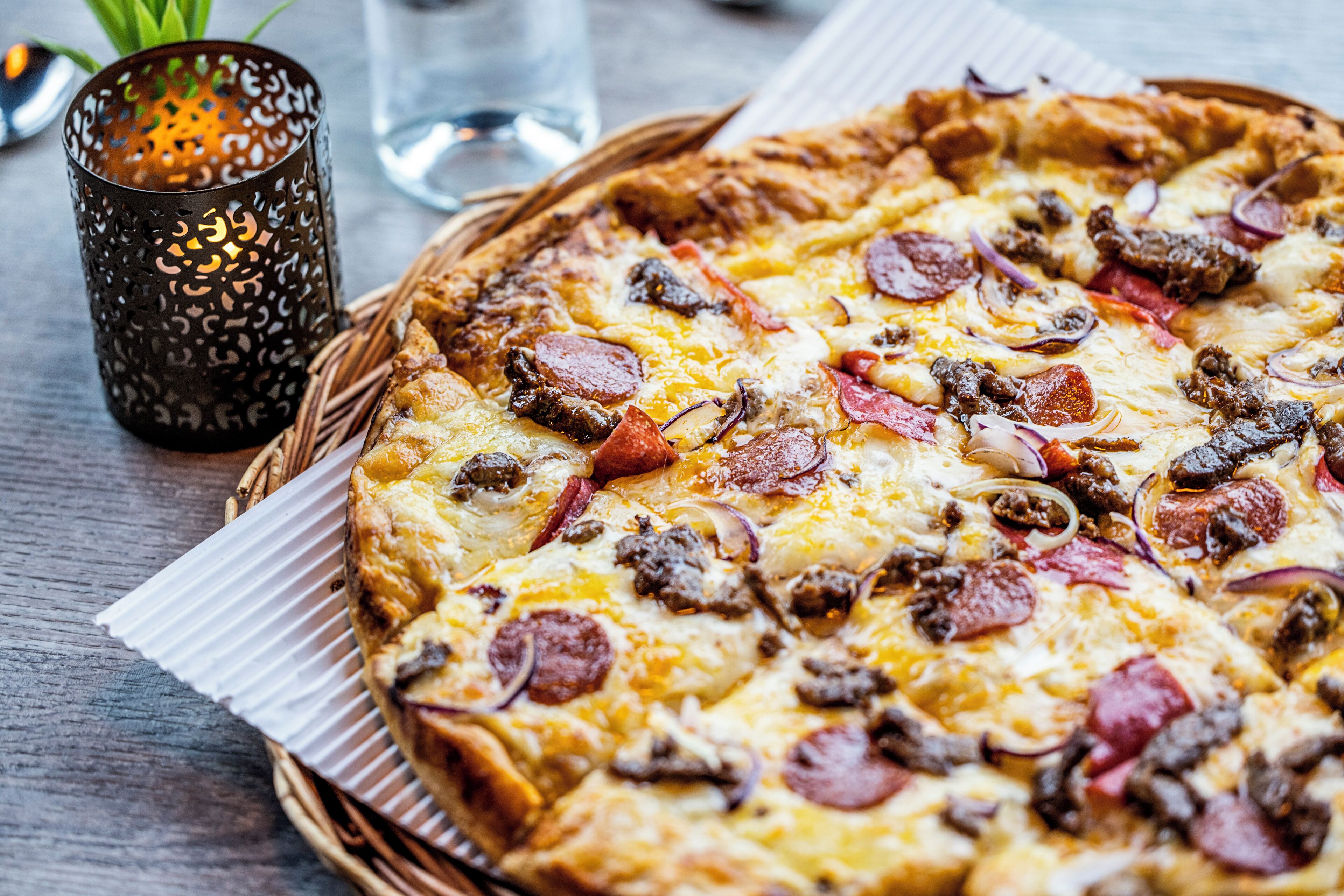 Eine Pizza mit verschiedenen Belägen, eine Kerze und ein Glas Wasser auf einem Tisch.