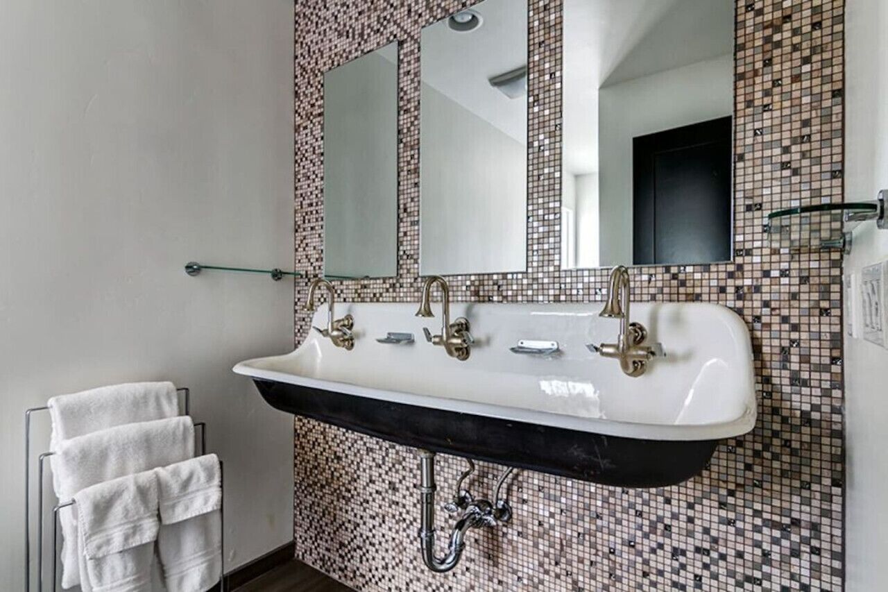Une salle de bain avec un lavabo blanc, deux miroirs et un mur recouvert de carreaux.