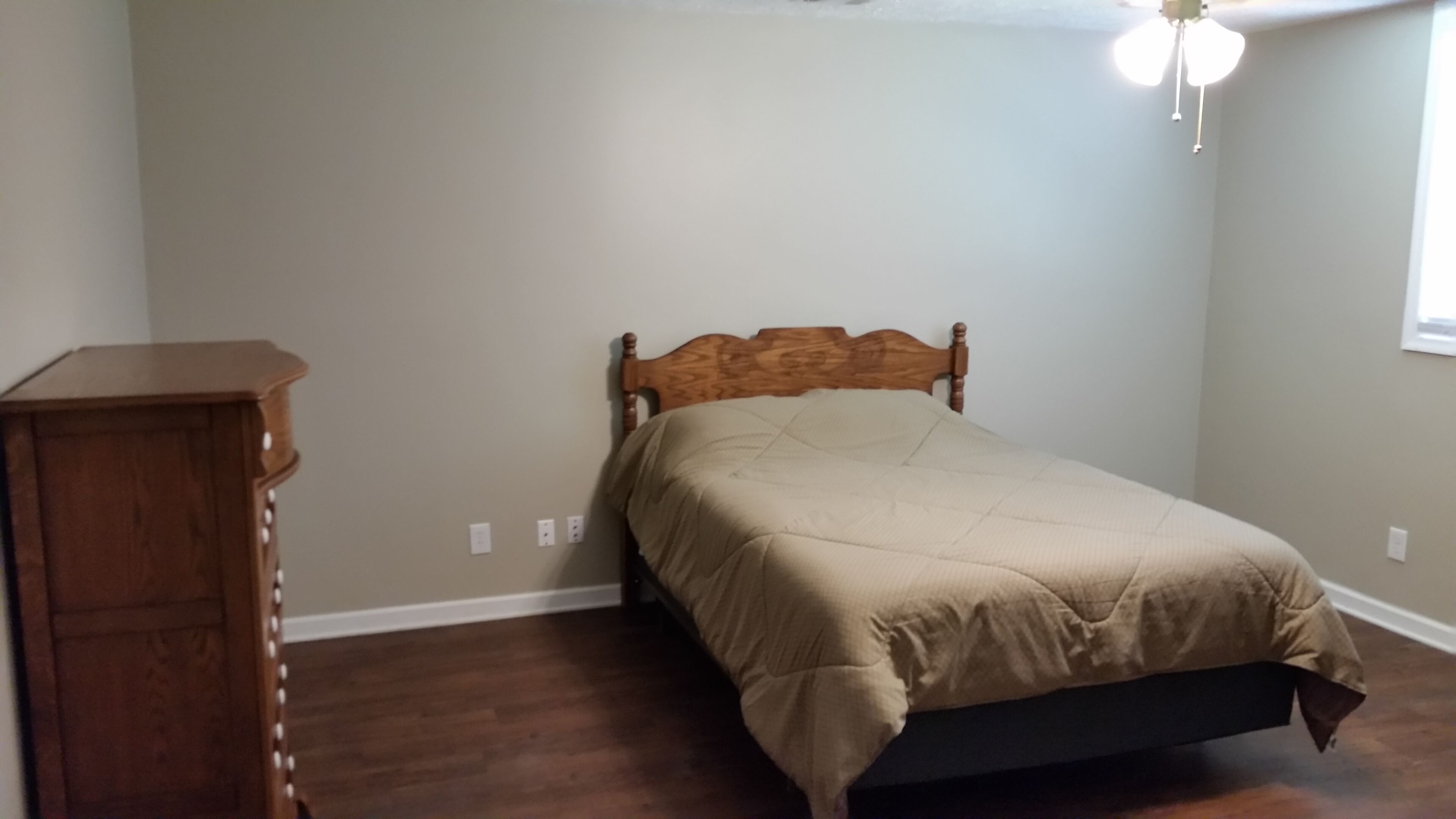 Un dormitorio con cabecera de madera, cama con colcha color beige, mesita de noche de madera y ventilador de techo.