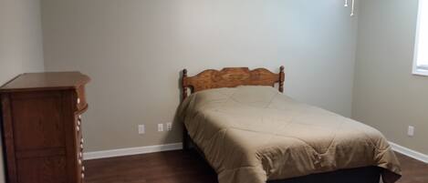 Un dormitorio con cabecera de madera, cama con colcha color beige, mesita de noche de madera y ventilador de techo.