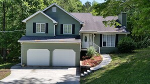 Een tweelaags huis met garage, een overdekte veranda en een aangelegde voortuin.