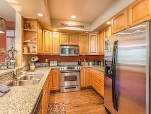 Kitchen features a refrigerator, microwave, double oven, and ample storage in wooden cabinets, along with a durable granite countertop and additional workspace.