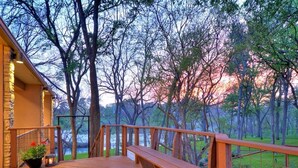 A wooden deck with a railing, a bench, and a stone building with a porch. - Spacious Riverfront Home (Martindale)