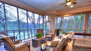 A sunroom with wicker furniture, a glass table, and a view of trees. - Spacious Riverfront Home (Martindale)