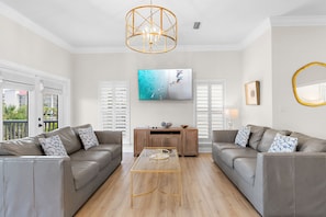 Un salon moderne avec un canapé gris, une table basse en verre, un meuble en bois et un grand téléviseur.