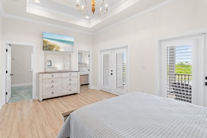 Une chambre avec un grand lit, une commode, un tableau et un balcon avec des volets.