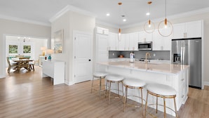 A modern kitchen with white cabinetry, stainless steel appliances, and a central island with bar stools.