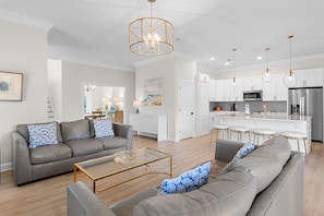 Ein modernes Wohnzimmer mit grauem Sofa, einem Couchtisch und einer Küchenzeile mit weißen Schränken und Edelstahlgeräten.