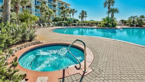 A hotel with a swimming pool, lounge chairs, and palm trees.