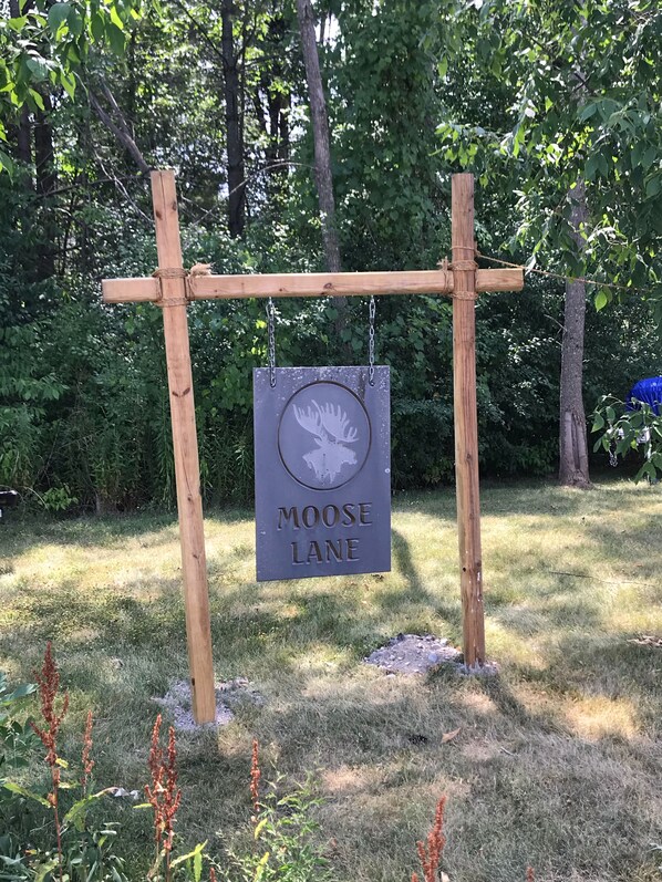 A wooden sign with a moose silhouette and the text "MOOSE LANE" hanging from a crossbeam structure. - Moose Lodge - Rustic and Cozy (Ticonderoga)